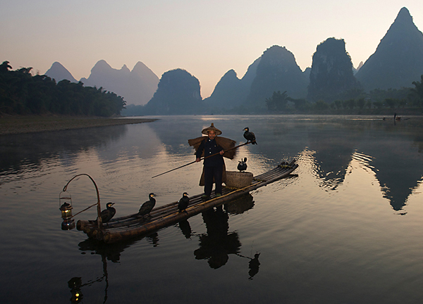 Cormorant fisherman on the Yulong river at dusk - near Yangshou, Guangxi Province, China Cormorant fisherman on the Yulong river at dusk near Yangshou, Guangxi Province, China